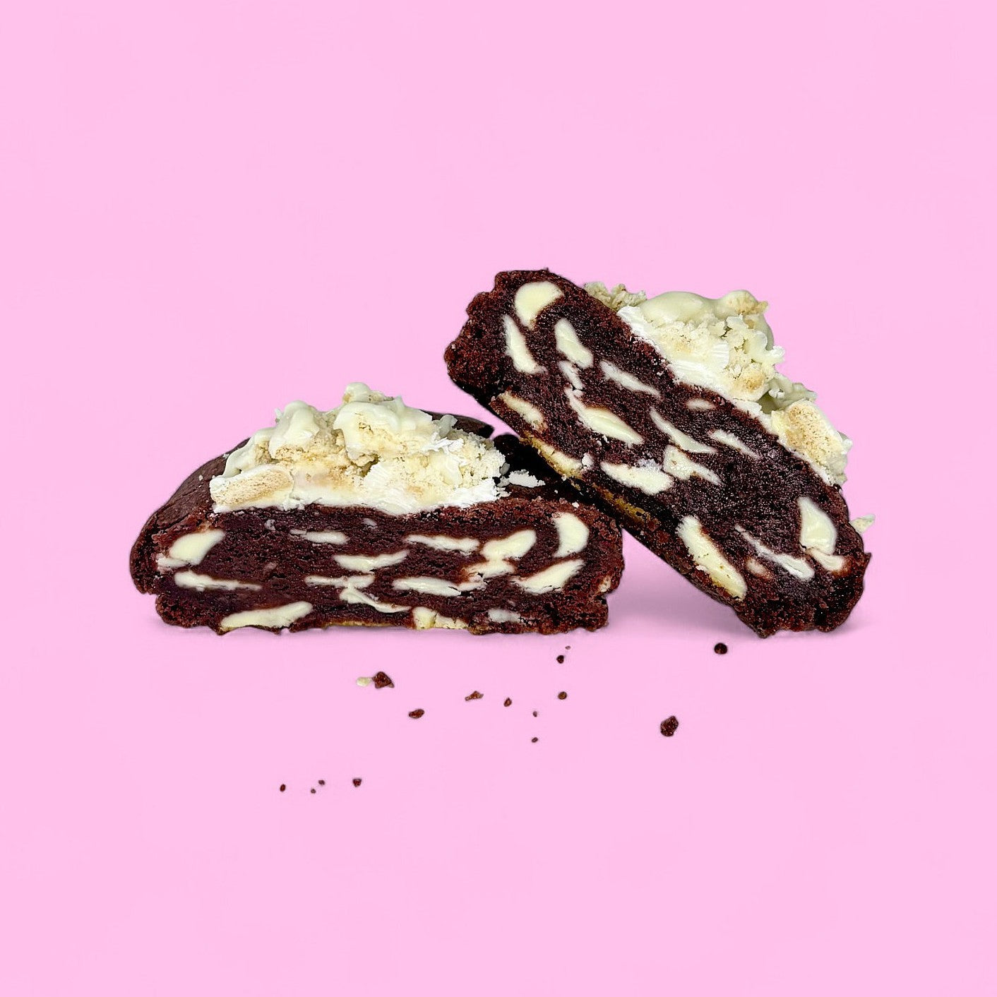 A dark red chunky cookie filled with white belgian chocolate on a pink background