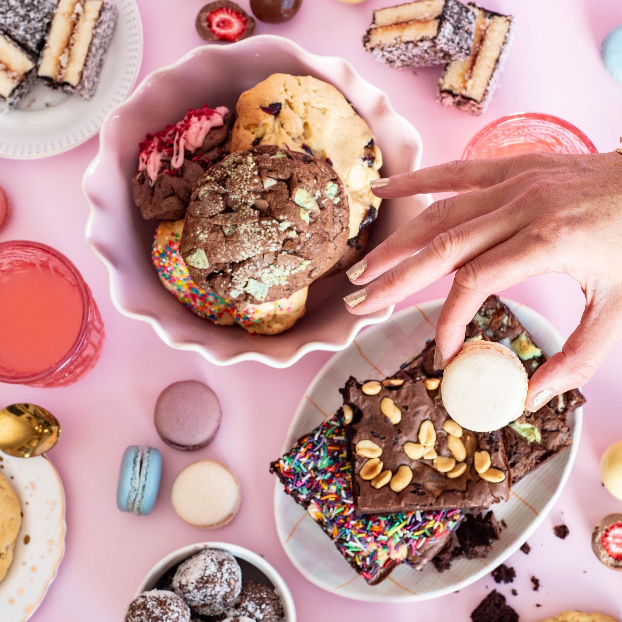 Mixed yummy desserts spread out on a table including, macaroons, rum balls, lamingtons, cookies and brownies