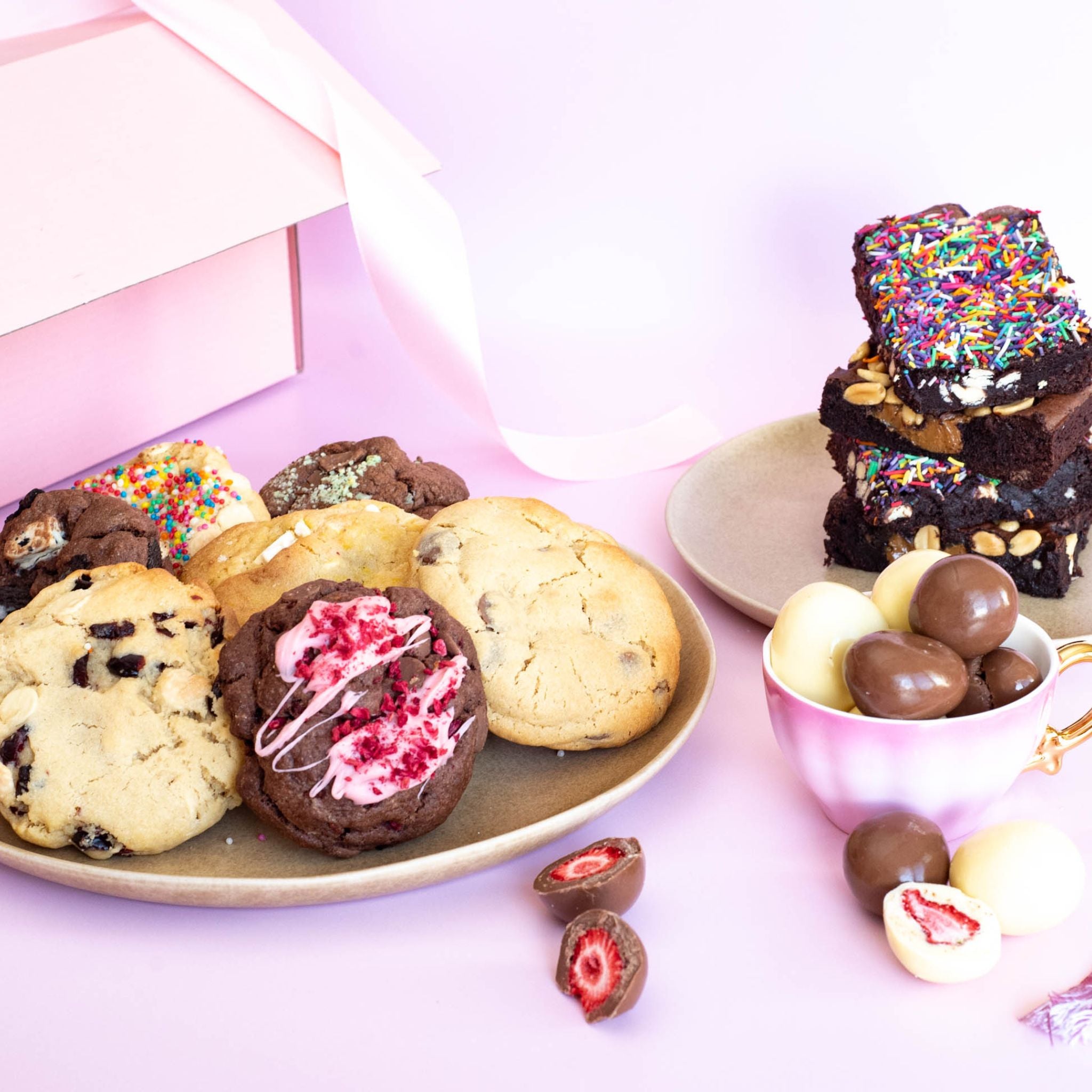 A pretty setup on handmade treats on a pink backdrop including brownies and cookies with colorful toppings and freeze-dried strawberries