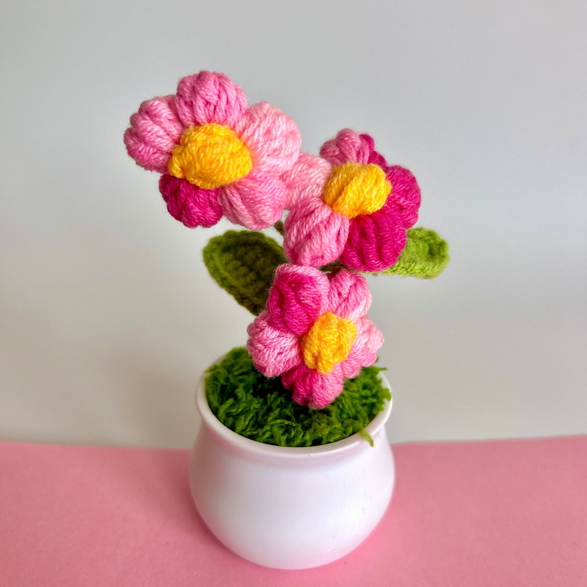 Multi colored pink hand knitted keepsake floral bouquet in a white pot