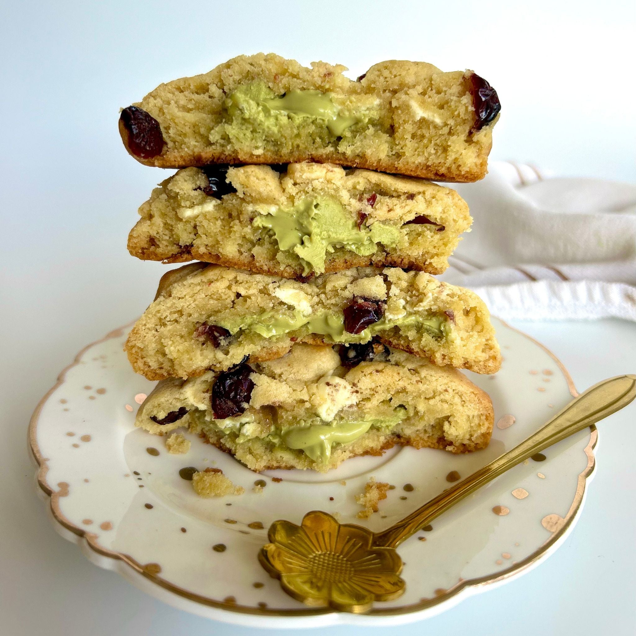 Delicious stacked pistachio papi cookies with cranberries and oozing pistachio spread on a white plate