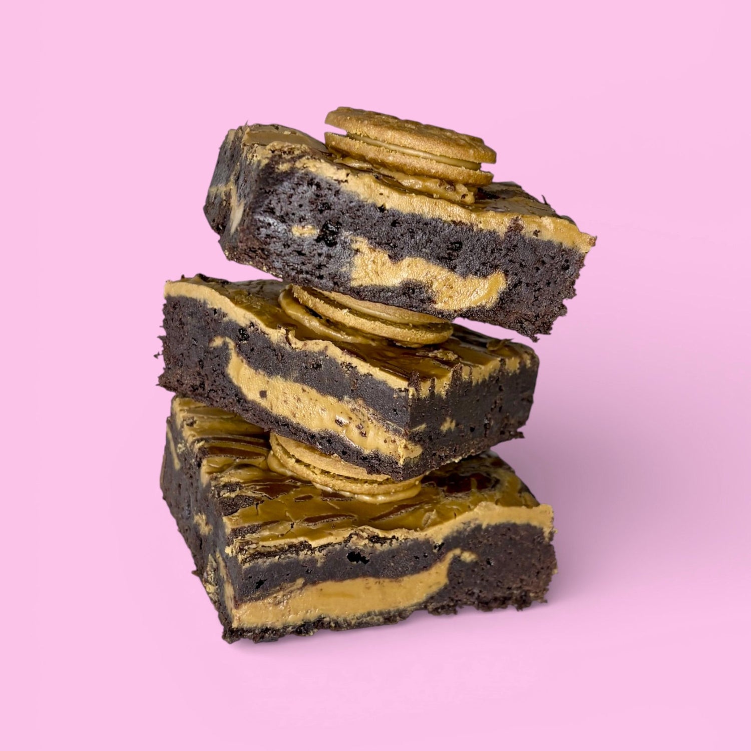 Stack of brownies featuring biscoff inside and on top, made with real belgian chocolate and shown against a pink background