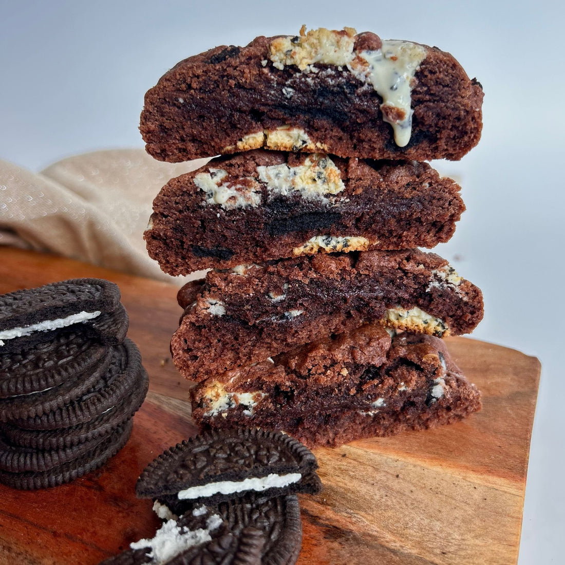 fresh baked cookies and cream oreo cookies cut in half to show melted chocolate oozing down the delicious chocolate dough cookie, sitting on a chopping board