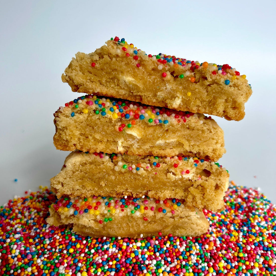 Side view of two funfetti cookies cut in half and stacked on top of each other on a base of sprinkles