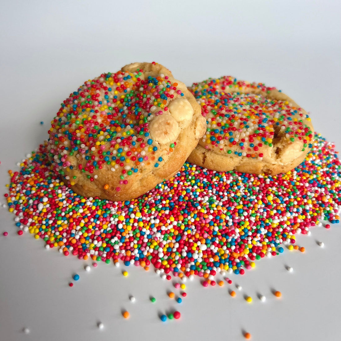 two rainbow sprinkle cookies sitting on top of a big pile of rainbow sprinkles or 100s and 1000s