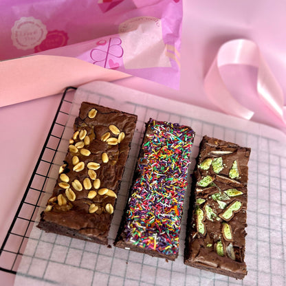 three individual brownies lined up side by side on baking paper next to a gift box hamper
