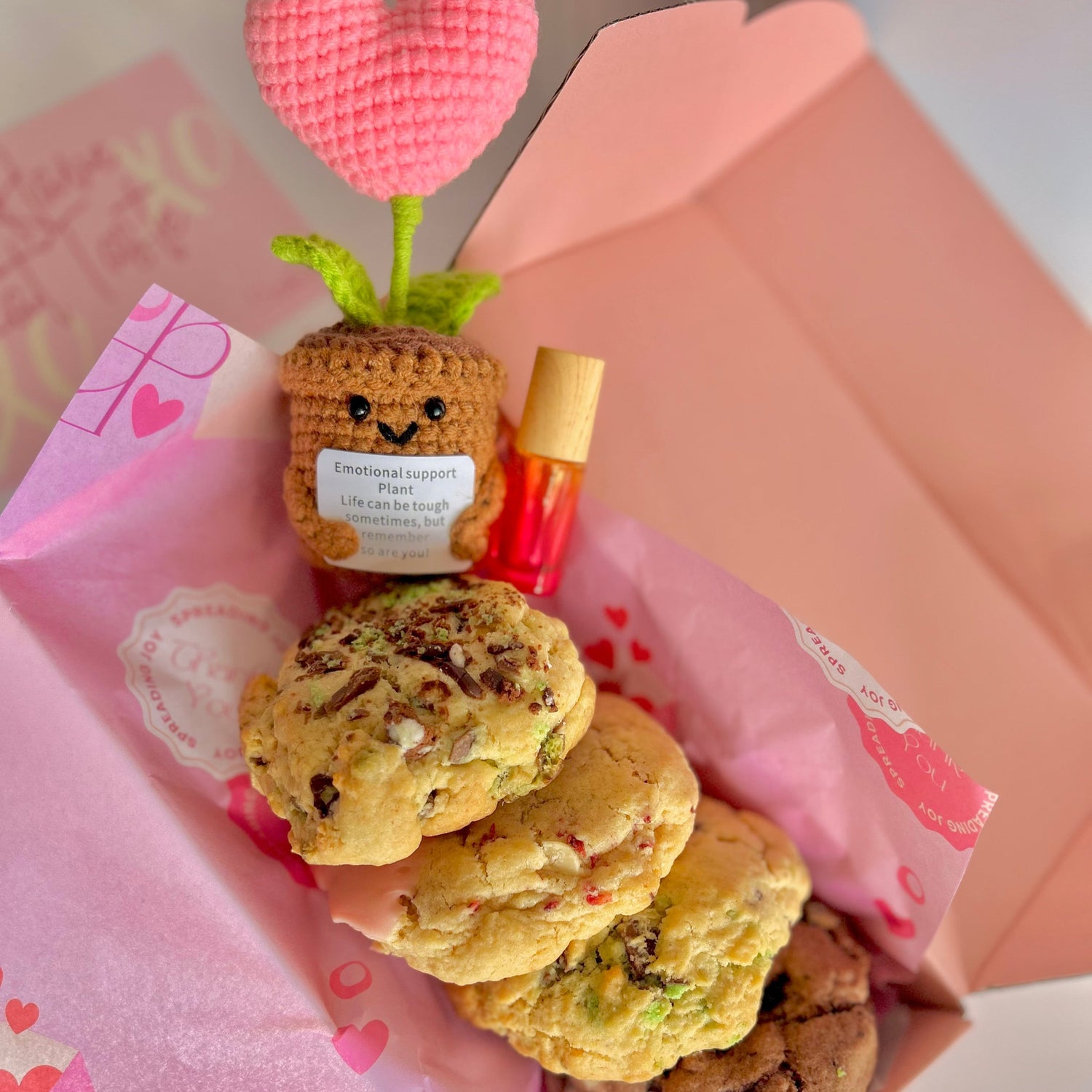 birds eye view of a knitted heart keepsake in a gift box with essential oil roller and 4 delicious cookies lined up ready for delivery
