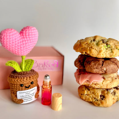 4 cookies stacked up with a knitted heart plant keepsake and an essential oil roller in front of a gift box ready for delivery