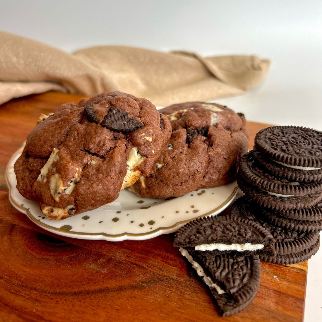 two chunky cookies with oreos and chocolate throughout sitting on a white plate with oreo biscuits in front