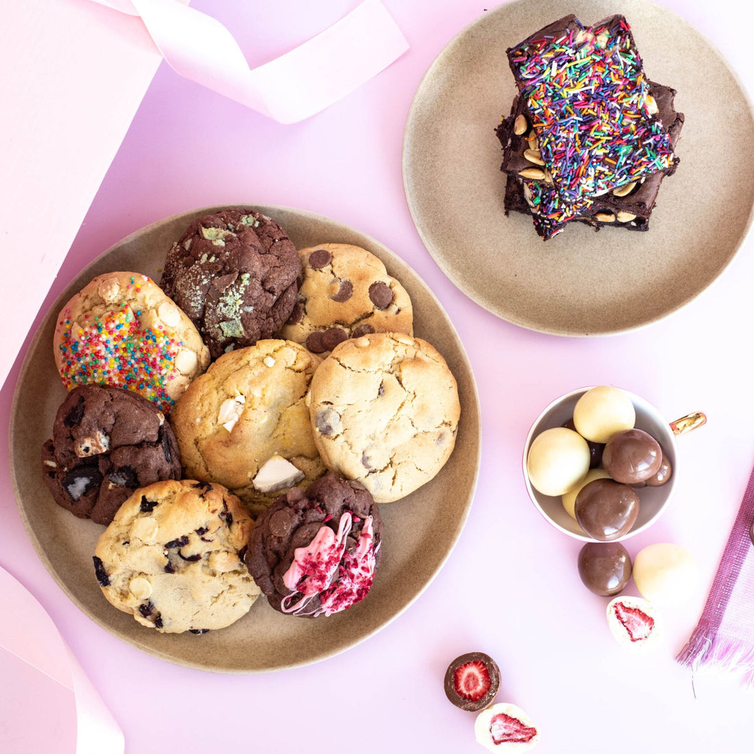 A mix of desserts including fresh baked cookies, chocolate brownies and chocolate covered strawberries displayed on plates and in cups on a pretty table cloth