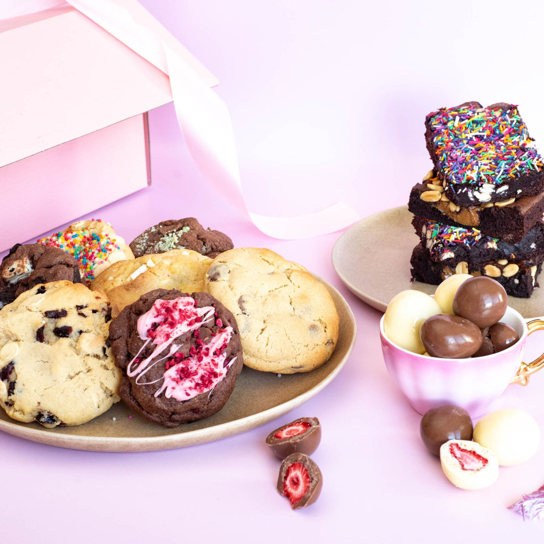 A pretty setup on handmade treats on a pink backdrop including brownies and cookies with colorful toppings and freeze-dried strawberries