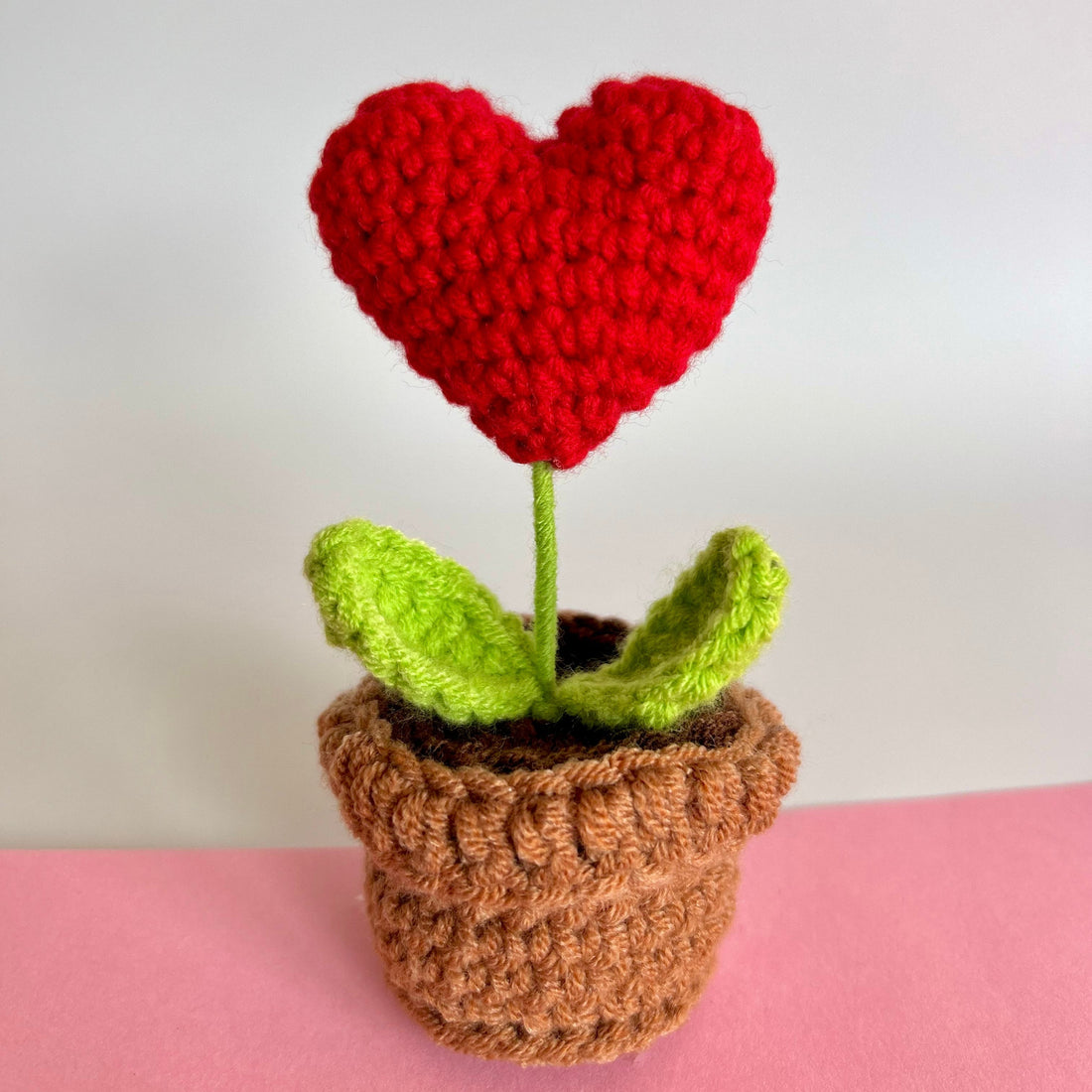 Hand knitted red heart shaped plant with green leaves and a brown pot