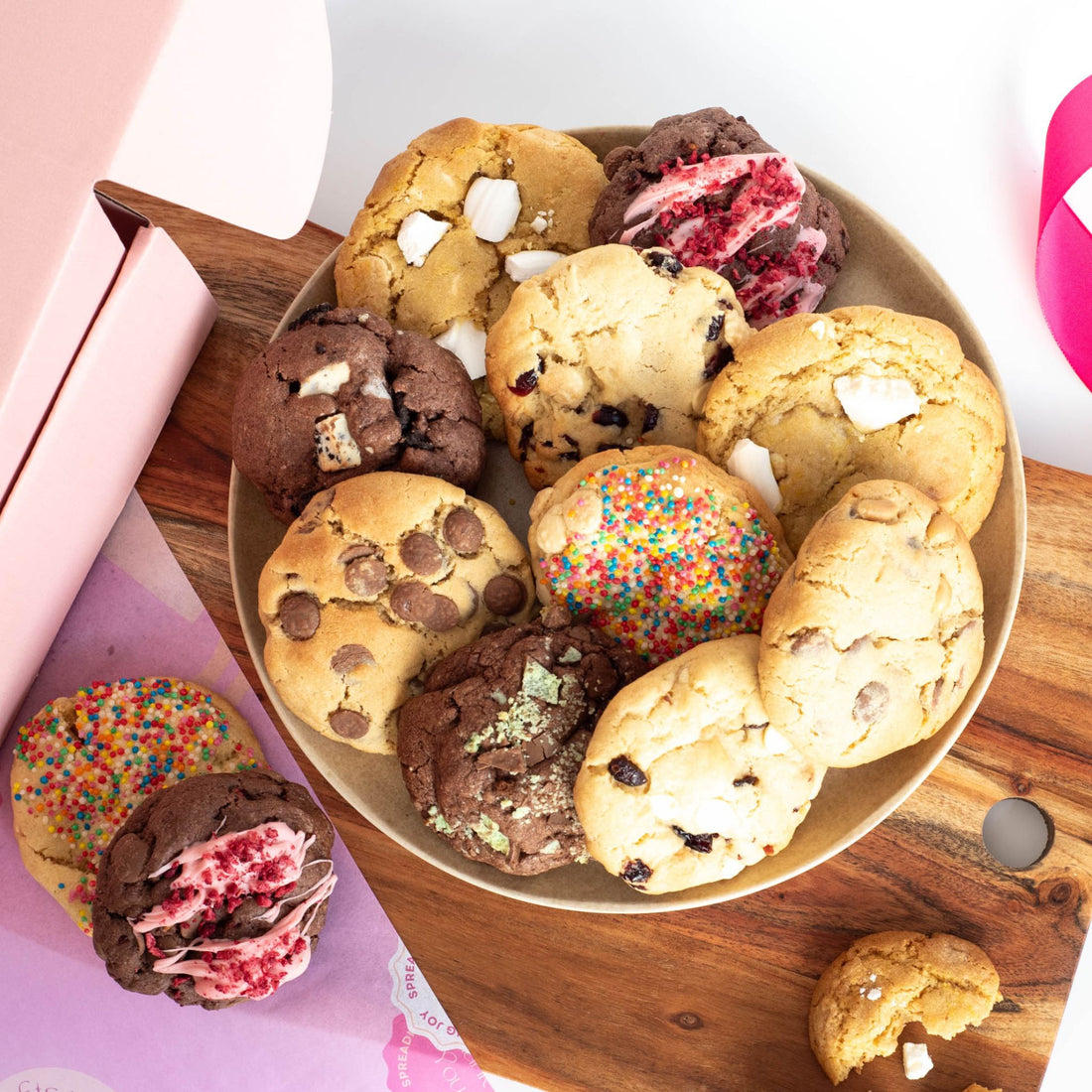 a plate with ten cookies of mixed variety on top, and two other cookies on a chopping board ready for a snack or party platter