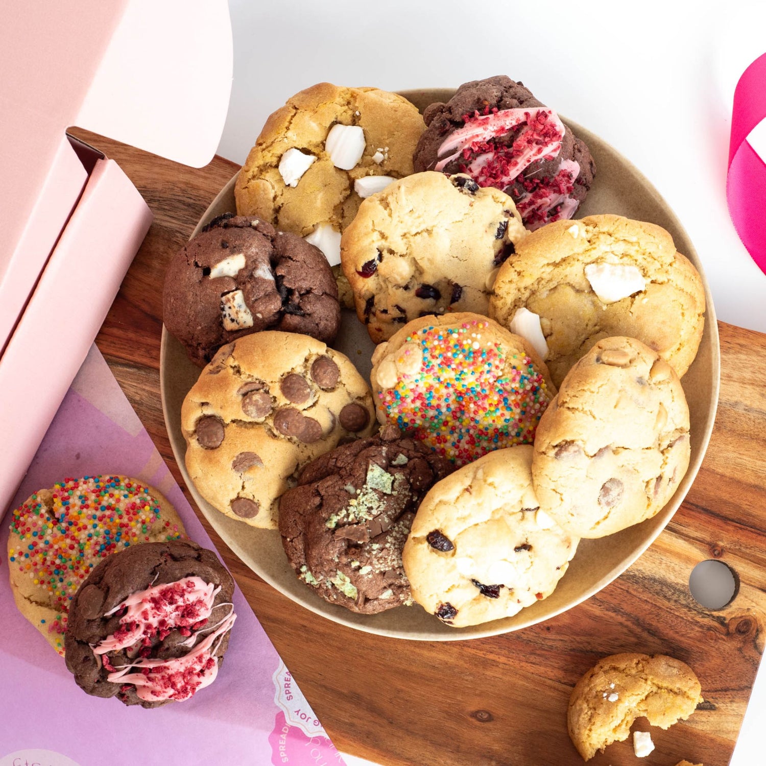 a plate with ten cookies of mixed variety on top, and two other cookies on a chopping board ready for a snack or party platter
