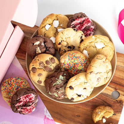 a plate with ten cookies of mixed variety on top, and two other cookies on a chopping board ready for a snack or party platter