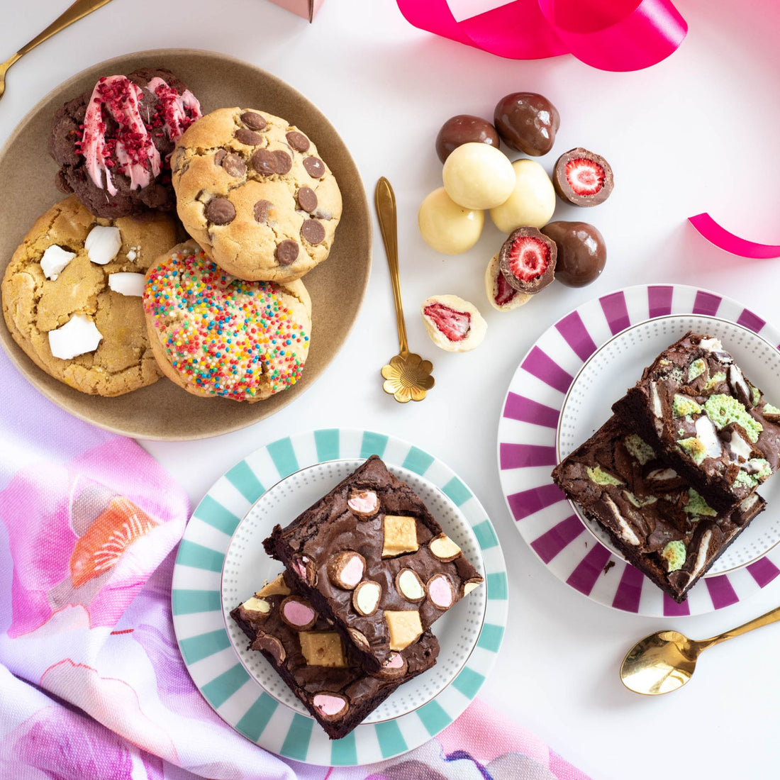 A colorful selection of handmade treats showcasing a plate of chunky cookies, two plates of mint brownies and caramilk brownies and hand-dipped strawberries