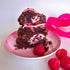 Cookies chopped in half sitting on a pink plate with pink ribbon in background. Cookies are chocolate dough with raspberry pieces throughout