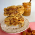 two peanut caramel cookies cut in half and stacked on top of each other on a white and gold plate, the middle of the cookie shows gooey caramel and golden peanuts with a jar of caramel in the background