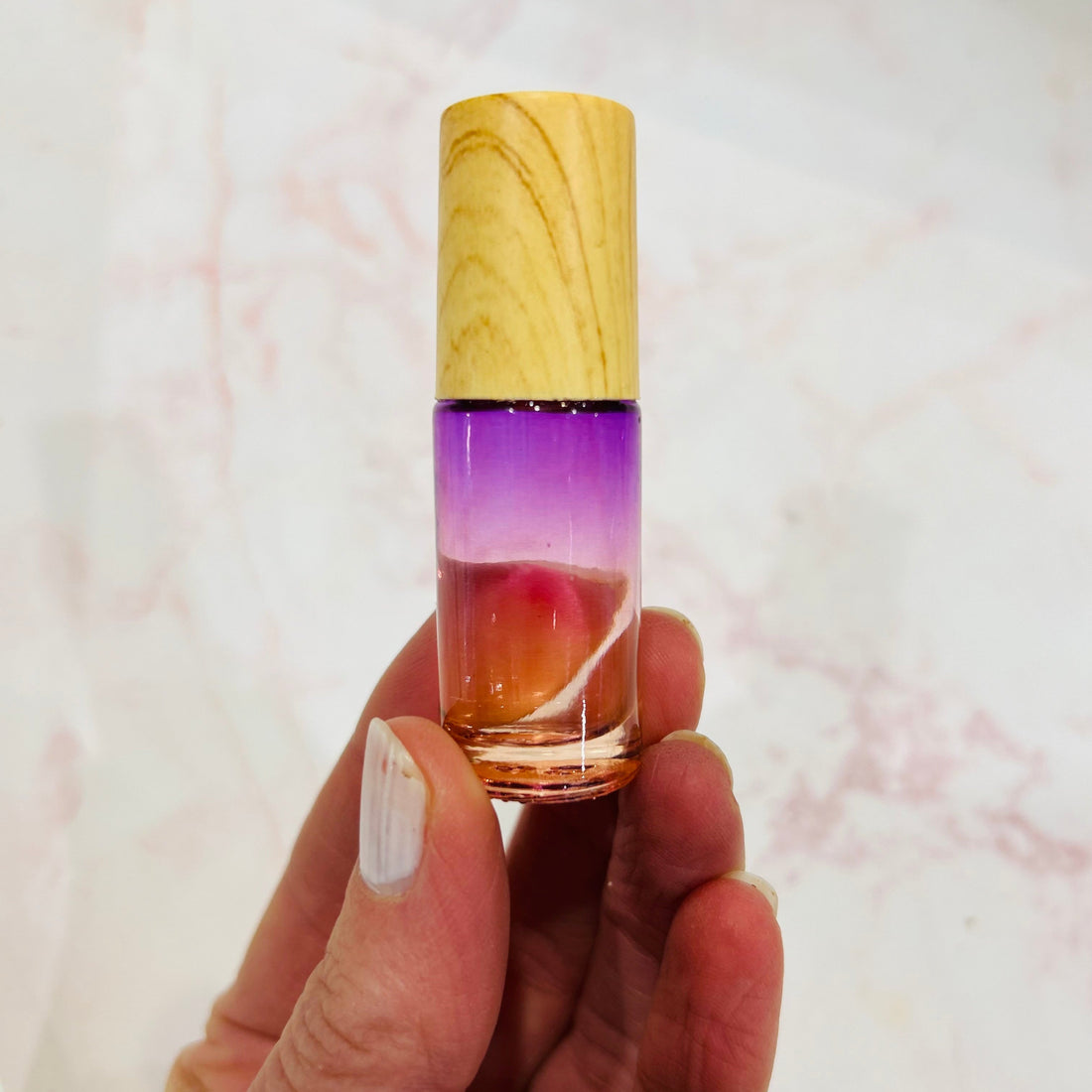 hand holding up a small roll-on vile of essential oil made of purple glass