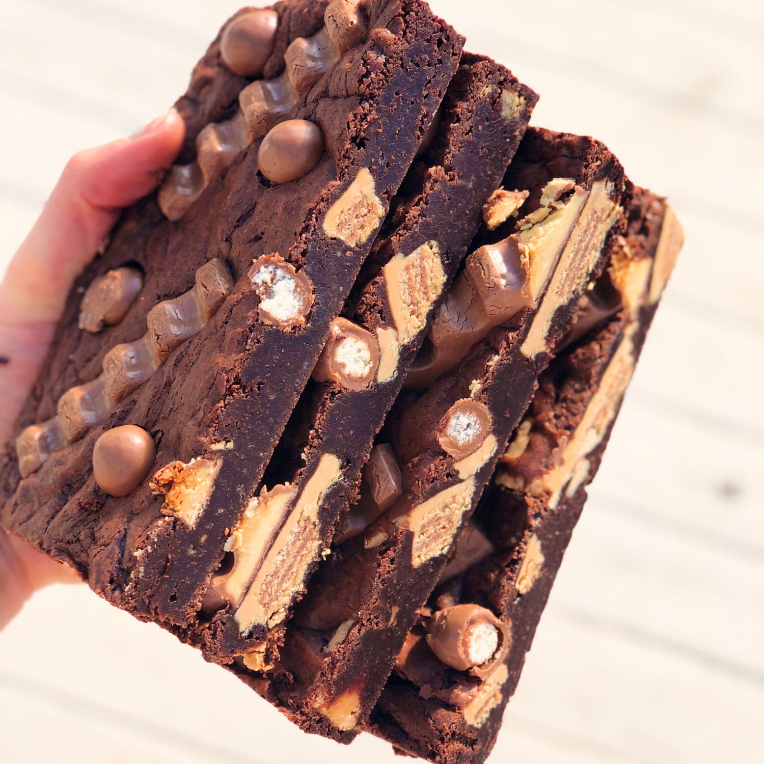 loaded brownies stacked with kitkat, maltesers and bueno held out by a hand