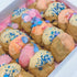 A gift box displayed with mini party birthday cookies in pink, yellow and orange colored icing with confetti